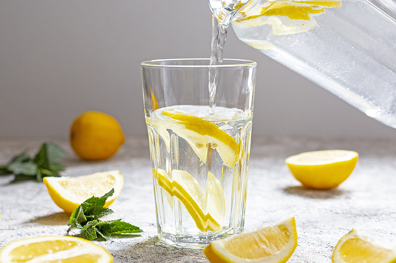 Water with lemon, mint and ice. Water is poured from a glass jug into a glass. Close-up.